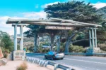 Car driving under Great Ocean Road entrance sign.